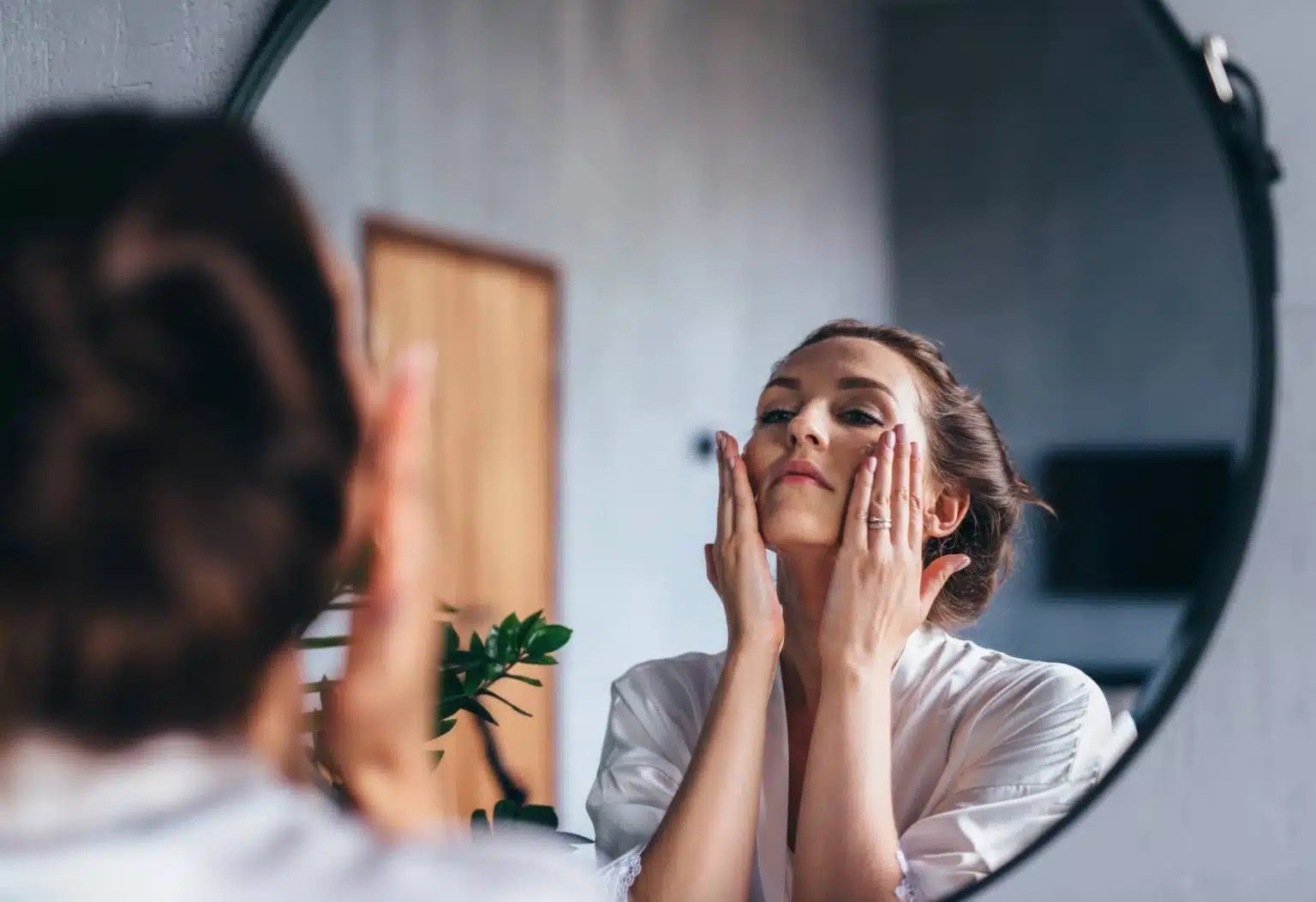 Mujer aplicándose crema facial frente a un espejo redondo en su rutina de mañana